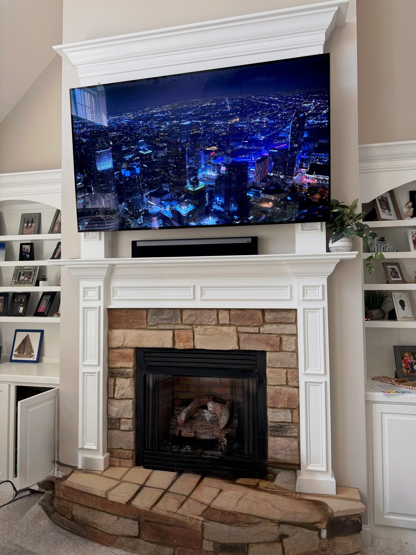 A television mounted above a stone fireplace, flanked by built-in white shelving.