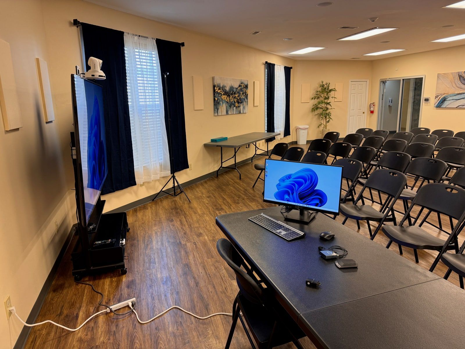 A community room set up with a mobile display cart, folding tables, and rows of chairs facing a presenter station.