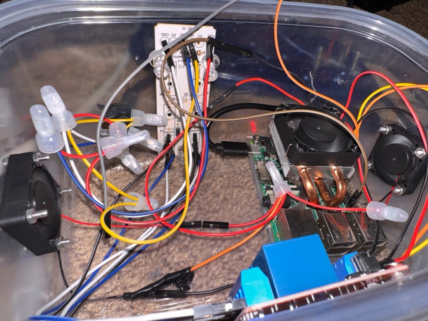 Inside a project enclosure showing a Raspberry Pi with a heatsink and fan, wired to speakers and an LED strip controller.