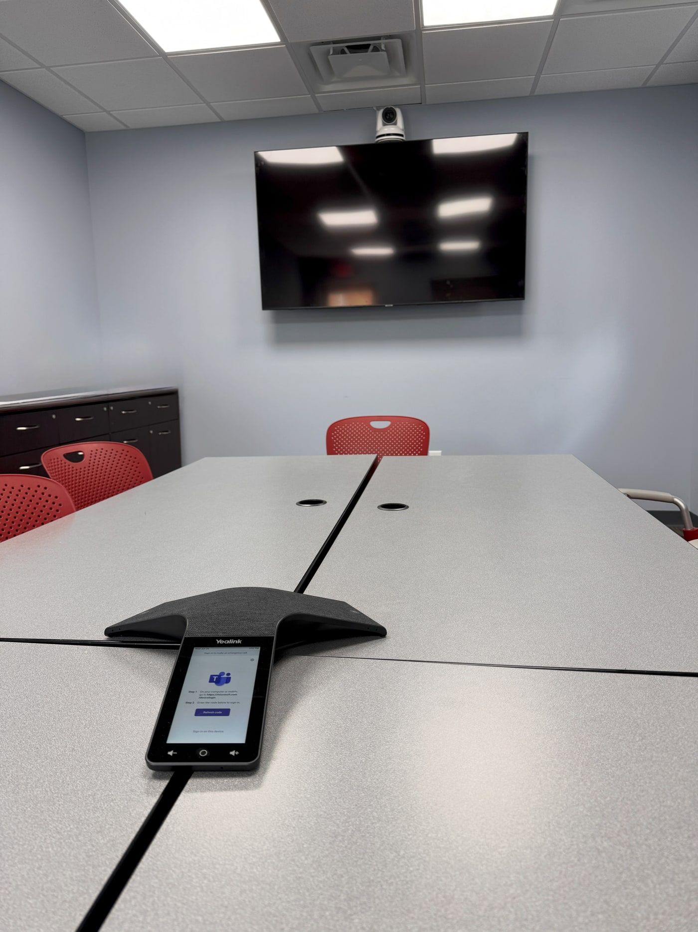 A portrait-oriented display mounted for video conferencing, with a PTZ camera on top, in a Teams meeting room.
